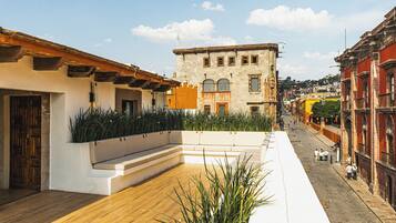 A rooftop terrace with a wooden floor, a white planter with plants, and a view of the street below.