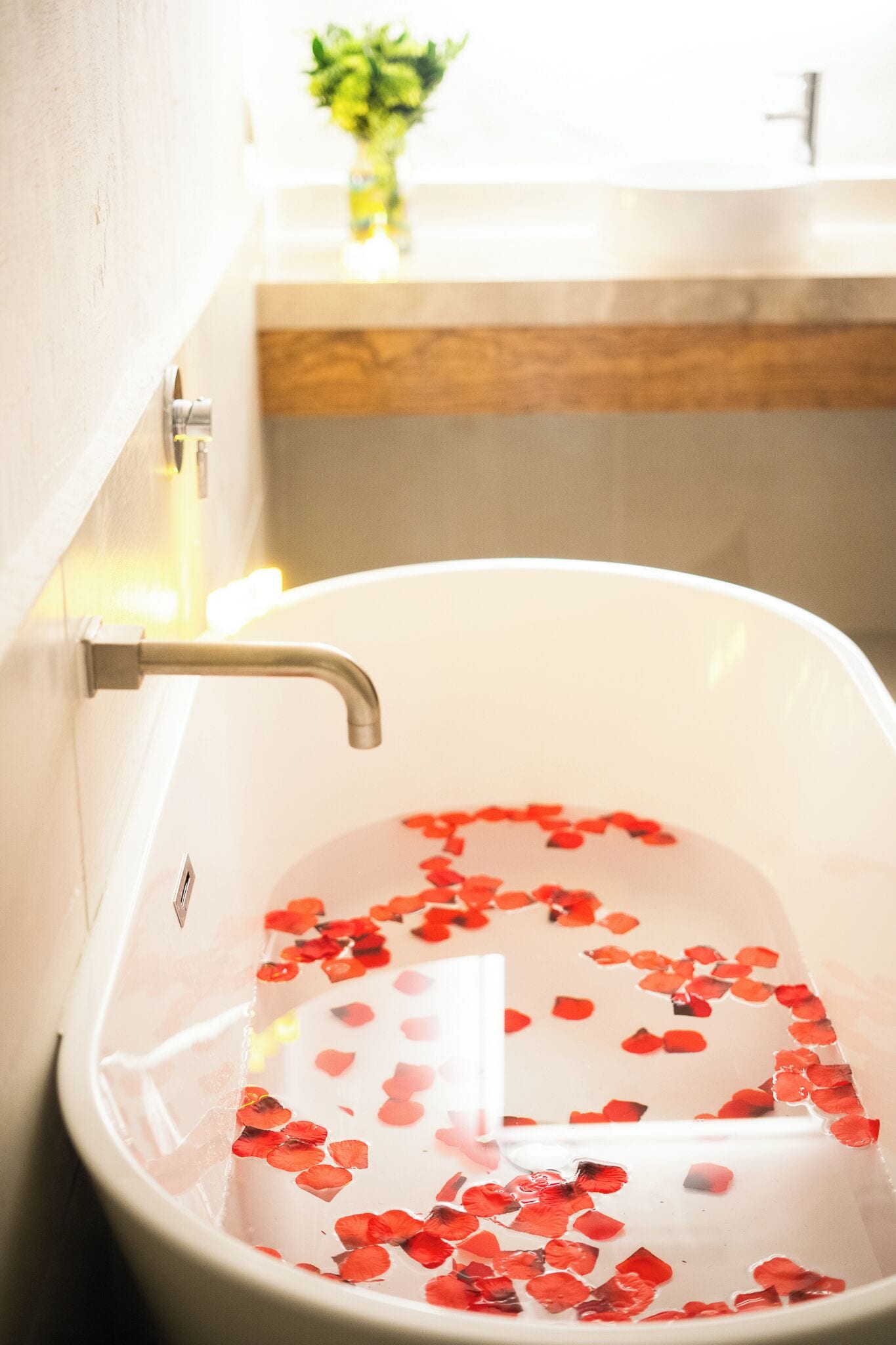 A bathtub filled with water and rose petals, a faucet, and a plant in the background.