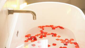 A bathtub filled with water and rose petals, a faucet, and a plant in the background.