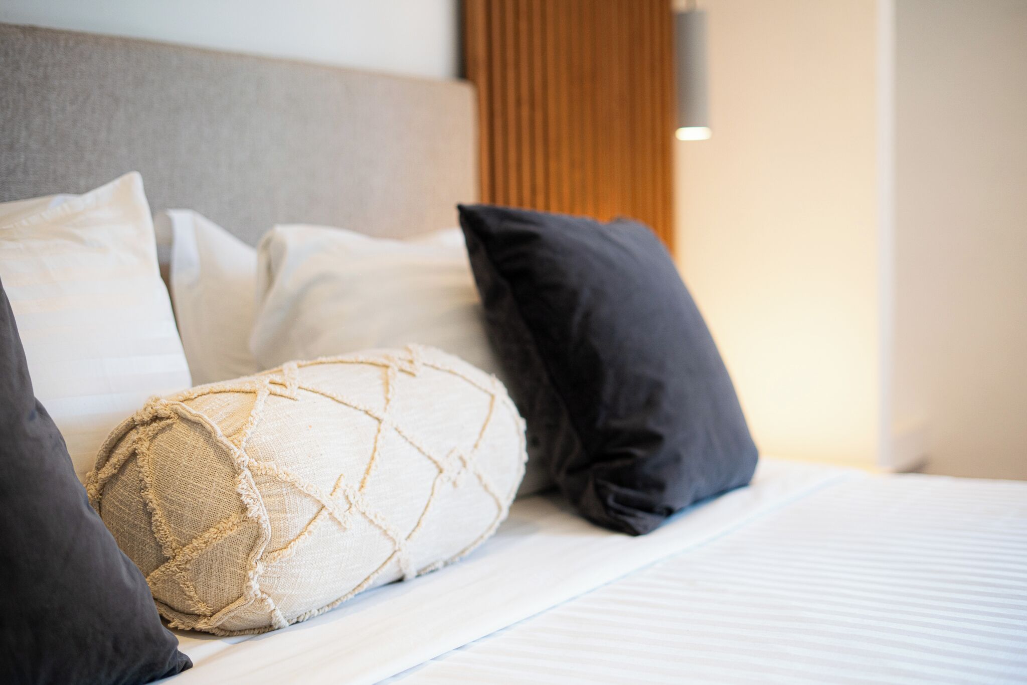 A neatly made bed with a variety of pillows, including a textured one and a couple of dark-colored ones.