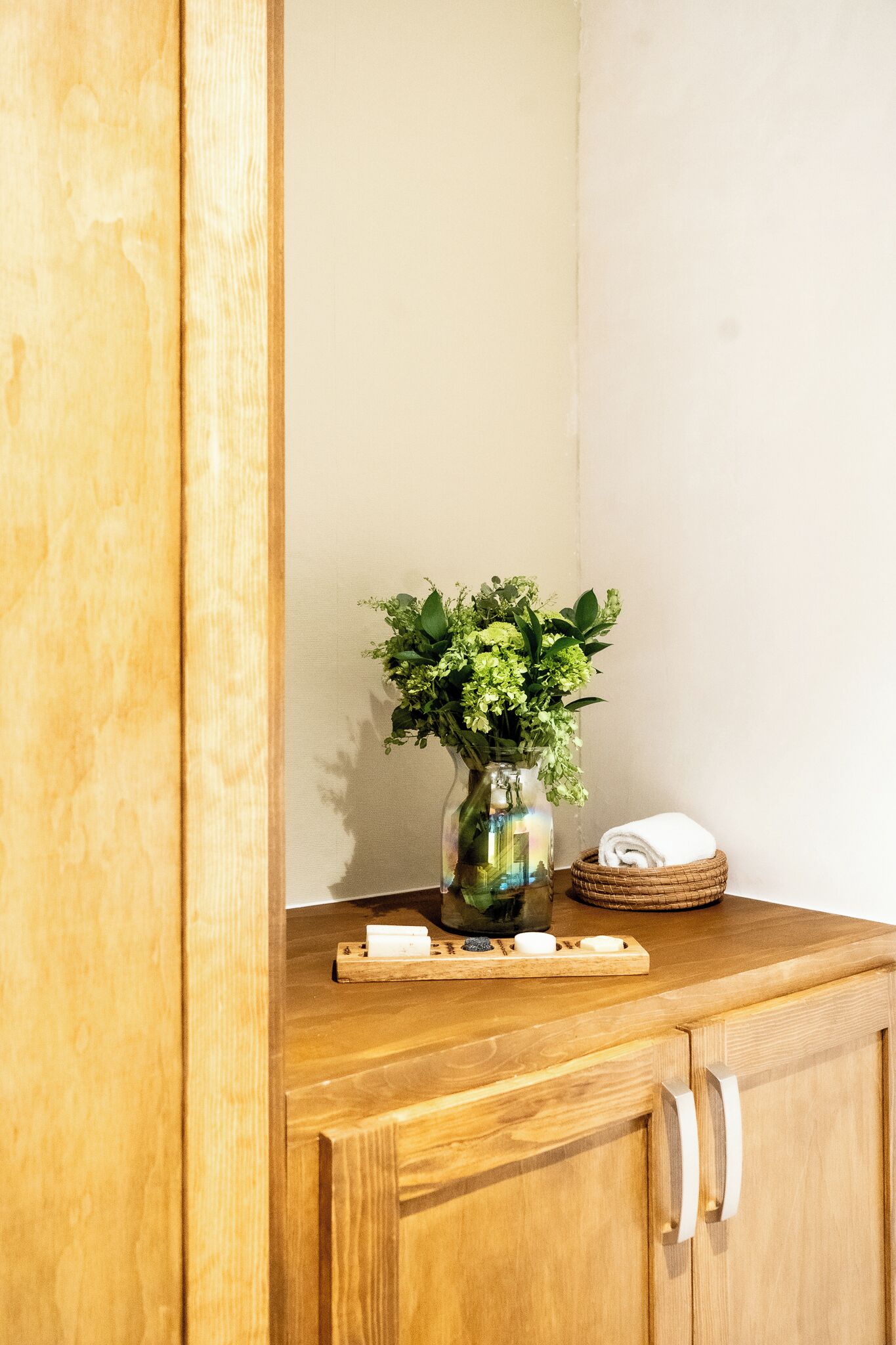 Ein Holzkabinent mit einer Blumenvase, einem gefalteten Handtuch und einer Ablage mit Seifenstücken.