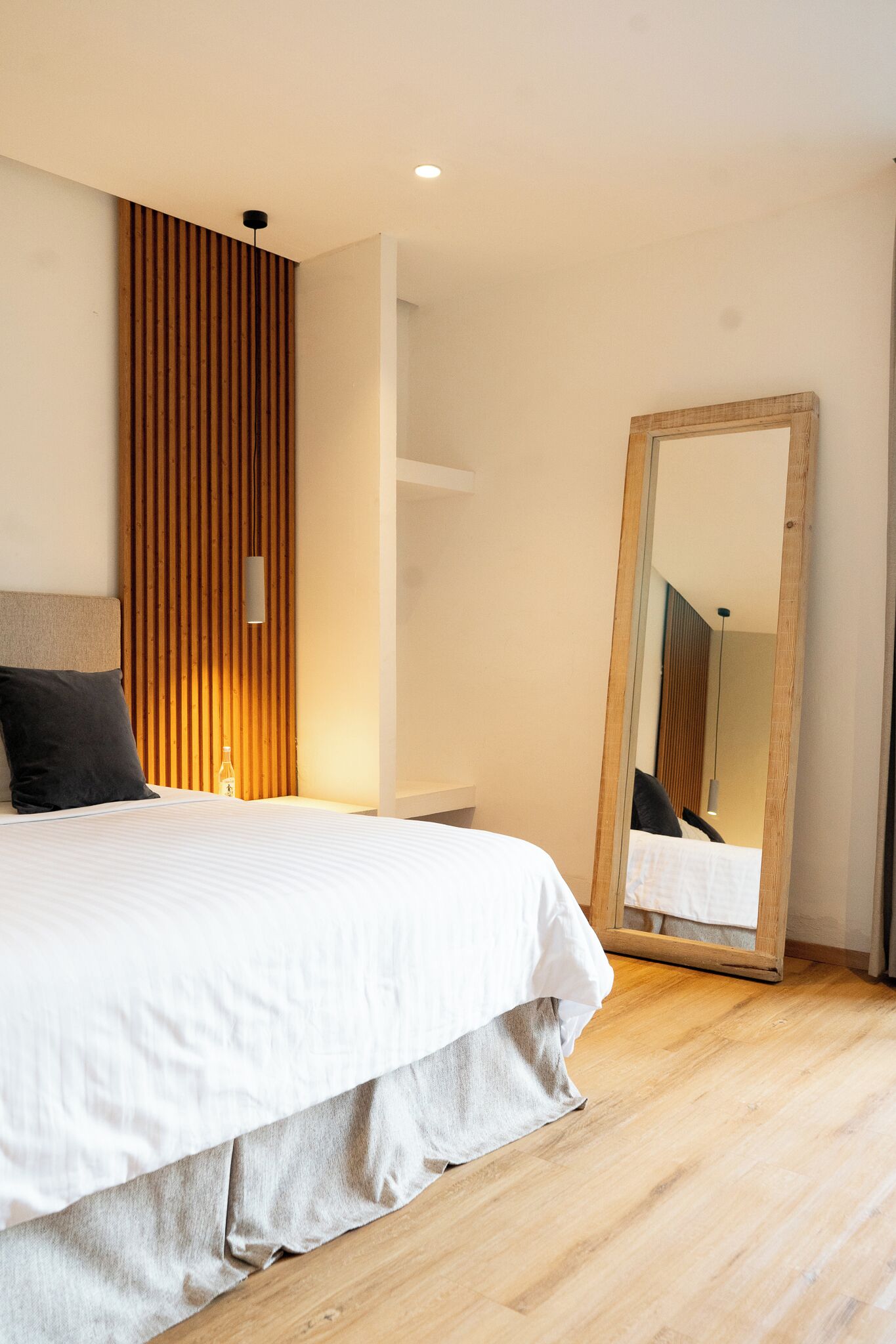 A modern bedroom with a wooden slat wall, a large mirror, and a neatly made bed.