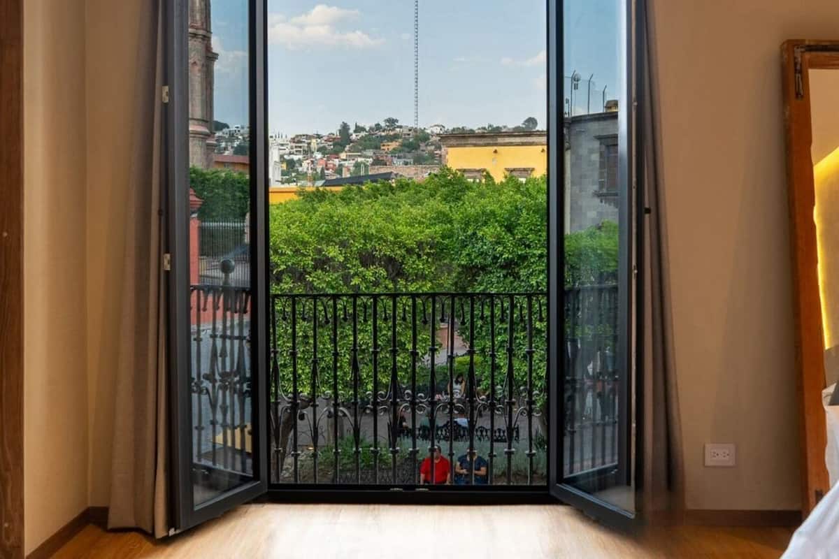 A room with a large sliding glass door leading to a balcony with a view of a cityscape and greenery.