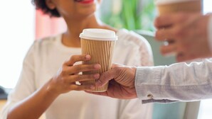 A person holding a paper cup, likely containing a beverage, with another person extending their hand towards it. - Hyatt Select Boston/Woburn/Burlington (Woburn)