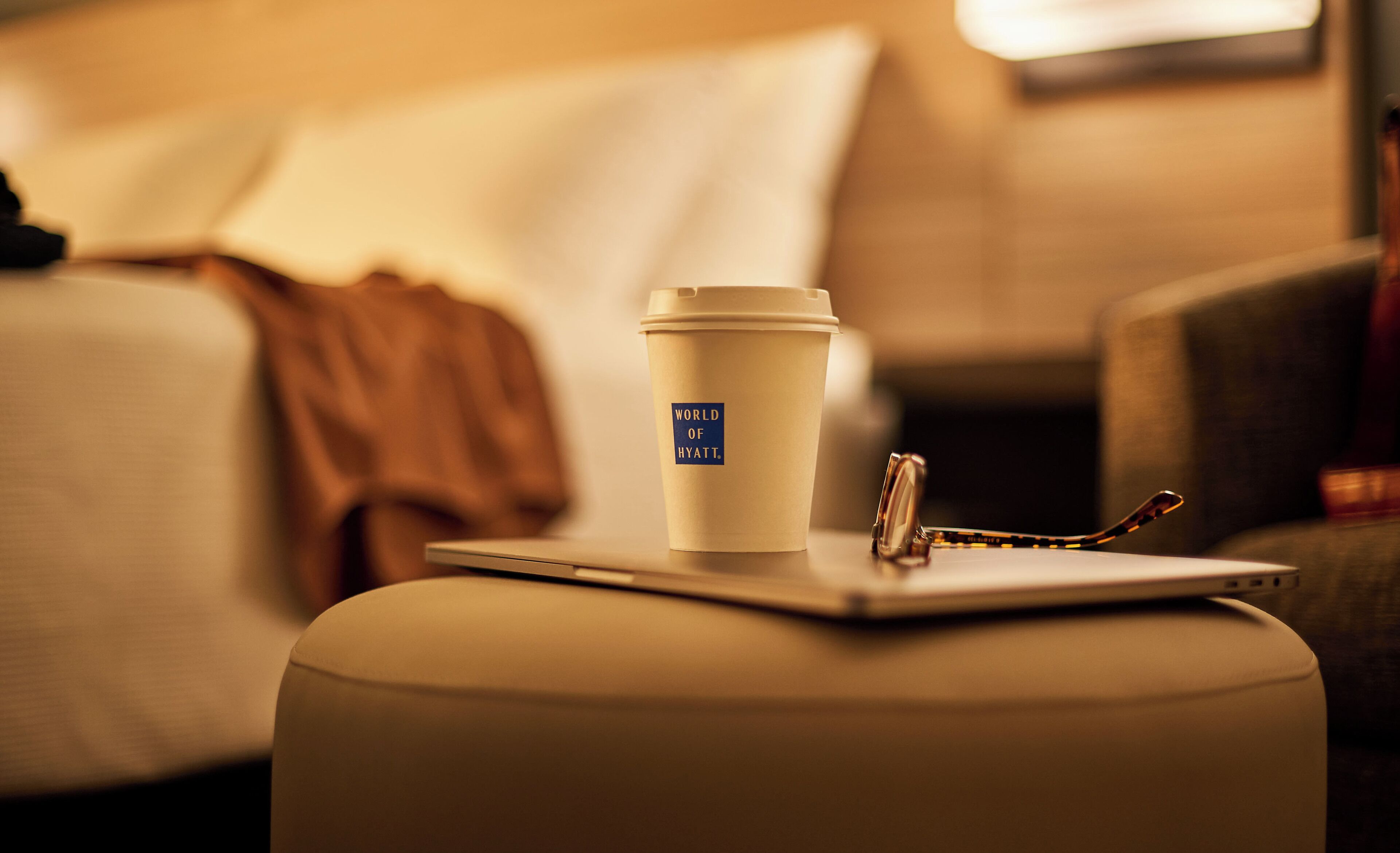 A cup with a lid and a pair of glasses on a table in a hotel room.