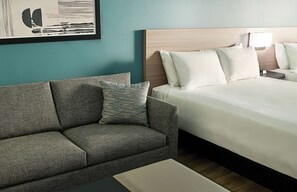 A hotel room with a bed, a sofa, a nightstand, a lamp, and a framed picture on the wall. - Hyatt Select Boston/Woburn/Burlington (Woburn)