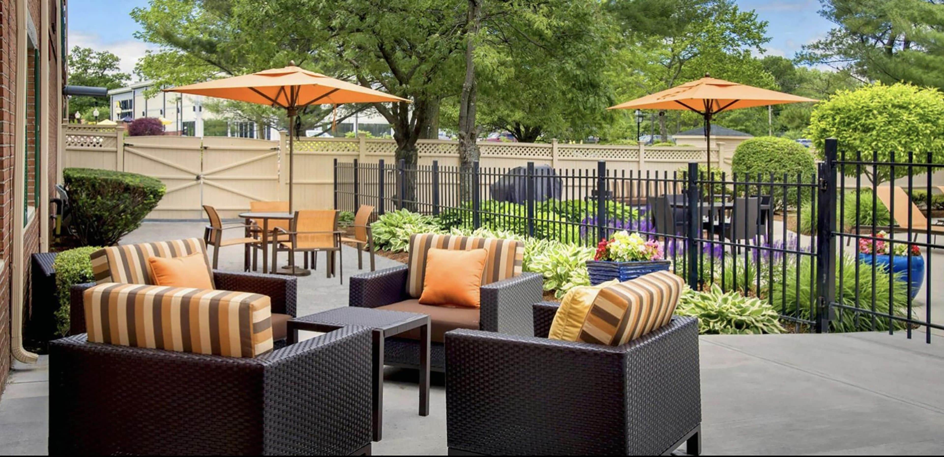 An outdoor patio with wicker furniture, orange umbrellas, and a fenced area with greenery.