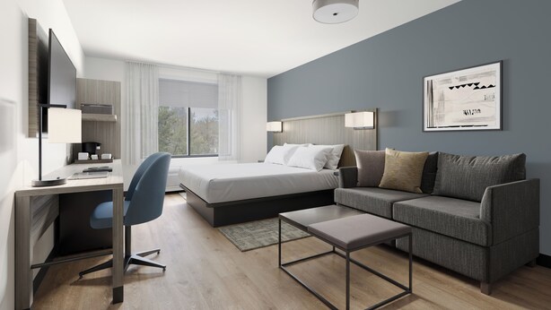 Una habitación de hotel moderna con cama, escritorio, silla, sofá y un cuadro enmarcado en la pared.