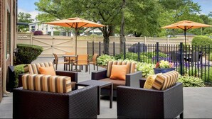 An outdoor patio with wicker furniture, orange umbrellas, and a fenced area with greenery. - Hyatt Select Boston/Woburn/Burlington (Woburn)
