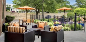 An outdoor patio with wicker furniture, orange umbrellas, and a fenced area with greenery. - Hyatt Select Boston/Woburn/Burlington (Woburn)