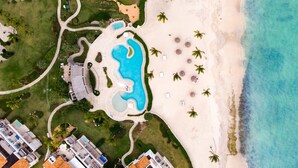 Vista aérea de un resort con una piscina central, varias villas para huéspedes y acceso a la playa.