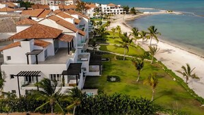 Un hotel frente al mar con varias construcciones, una playa y palmeras.
