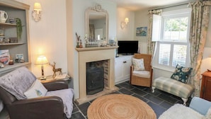 A cozy living room with a fireplace, a television, and comfortable seating. - Woodbine Cottage (Whitby)