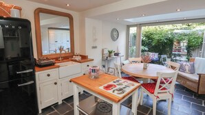 A modern kitchen with a black refrigerator, white cabinets, and a wooden countertop. There is a dining area with a round table and chairs, and a view of the garden through large windows. - Woodbine Cottage (Whitby)