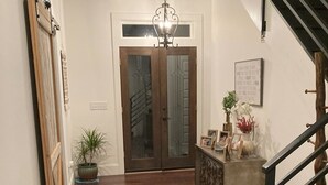 A hallway with a wooden floor, a staircase with a black railing, a chandelier, and a door with glass panels. - Charming 3-bedroom farmhouse with Pool &Hot Tub in Asheville Fletcher area (Fletcher)