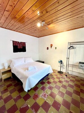 A bedroom with a bed, a nightstand, a wall-mounted fan, and a checkered floor. - Casa ELA Cuarta (Antigua Guatemala)