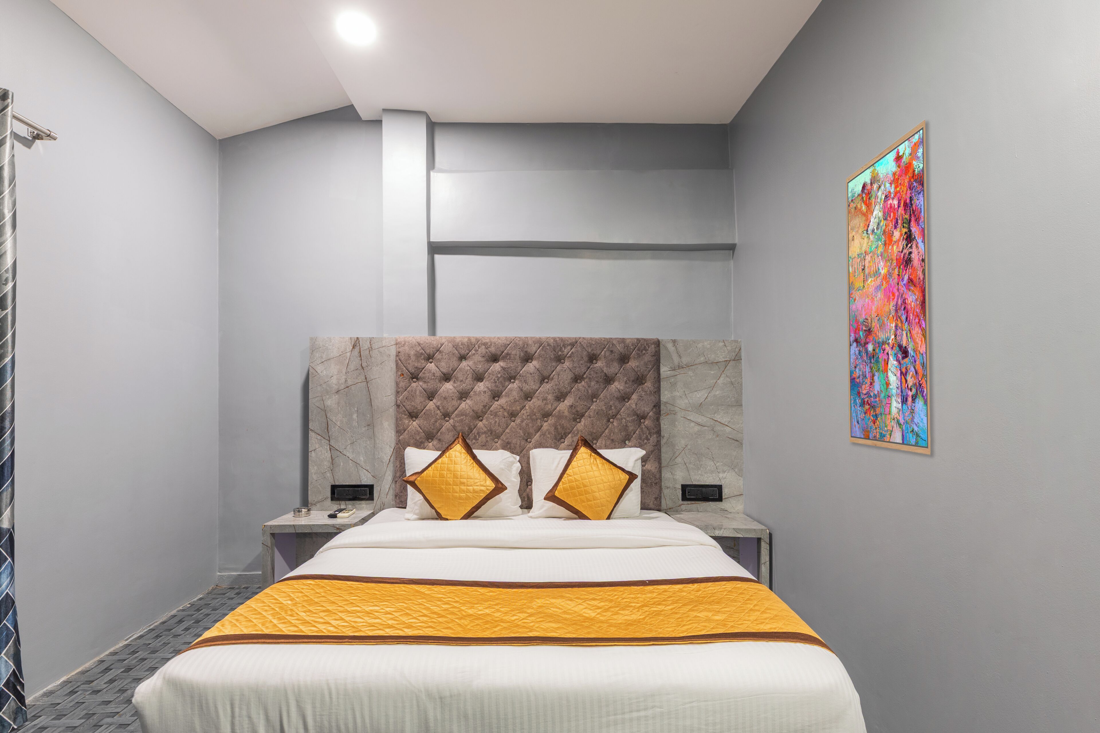 A modern hotel room with a large bed, a marble headboard, and a colorful abstract painting on the wall.