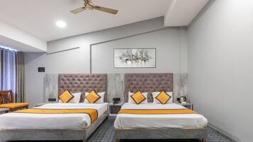 A hotel room with two beds, a ceiling fan, a cityscape artwork, and a marble headboard.