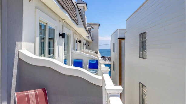 A narrow corridor with white walls and blue chairs, leading to a pool area with a view of the sea. - 3BR Seaside Haven - Beach Block Home w/ Parking (Seaside Heights)