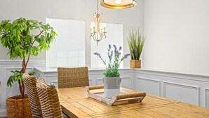 A dining area with a wooden table, wicker chairs, a chandelier, and potted plants. - 3BR Seaside Haven - Beach Block Home w/ Parking (Seaside Heights)