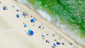 An aerial view of a beach with people, umbrellas, and beach chairs. - 3BR Seaside Haven - Beach Block Home w/ Parking (Seaside Heights)