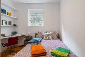 A bedroom with a bed, a desk, a chair, and a window.