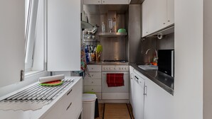 Une cuisine compacte équipée d’une cuisinière, d’un four et d’un évier, d’une fenêtre avec des rideaux et d’une petite poubelle.