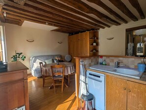 A compact kitchen with wooden beams, a dining area with a table and chairs, and a built-in dishwasher.