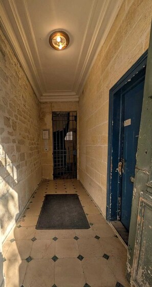 A narrow hallway with a tiled floor, a blue door, and a light fixture on the ceiling.