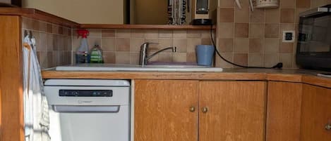 A compact kitchen with wooden cabinets, a built-in dishwasher, and a striped rug.