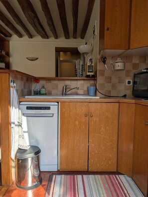 A compact kitchen with wooden cabinets, a built-in dishwasher, and a striped rug.