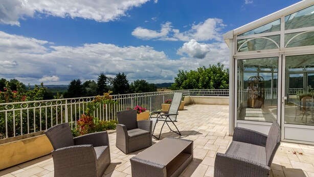 A terrace with wicker furniture, a glass-enclosed area, and a view of the landscape. - Guest Room in Vignols (Vignols)
