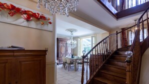 A wooden staircase with a chandelier, a dining area with chairs, and a wall with a floral painting. - Guest Room in Vignols (Vignols)