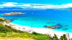A beach with clear turquoise waters, a sailboat, and rocky outcrops. - A CASA DEL BOSQUE DEL AGUA+PASE A SPA PREXIGUEIRO GRATIS A PARTIR DE 01.09.2025 (MONDARIZ)