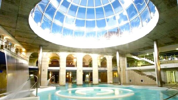 An indoor swimming pool with a glass ceiling, multiple levels, and a central circular water feature. - A CASA DEL BOSQUE DEL AGUA+PASE A SPA PREXIGUEIRO GRATIS A PARTIR DE 01.09.2025 (MONDARIZ)
