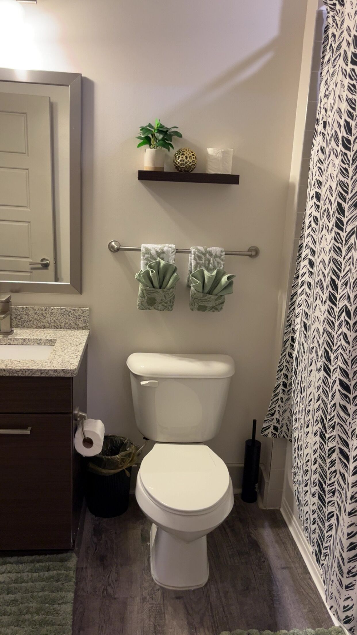 A bathroom with a toilet, a shelf with a plant and decorative items, and a towel rack with folded towels.