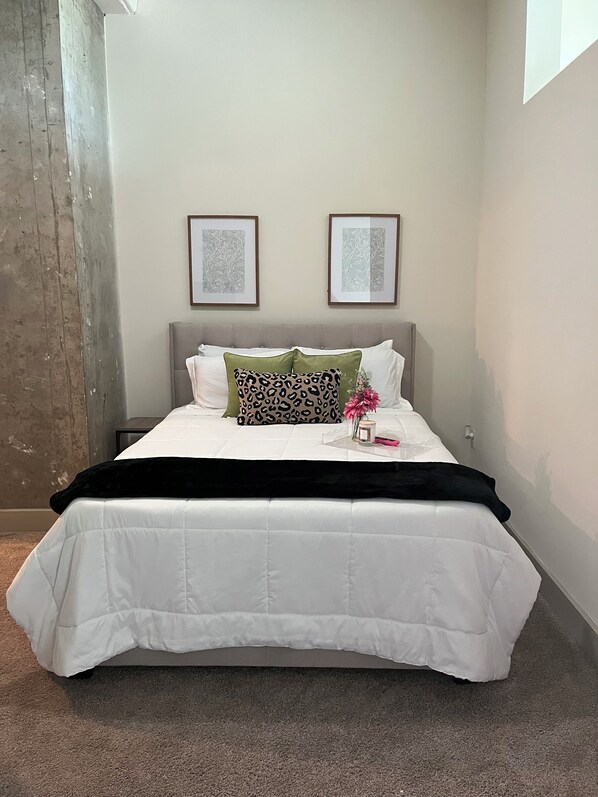 A neatly made bed with white bedding and a black throw blanket, two leopard print pillows, and a vase with pink flowers on a bedside table.