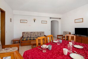 Un comedor con mantel rojo, sillas de madera, un sofá y una televisión.