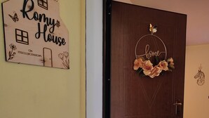 A wooden door with a 'Home' sign and a welcome mat. A 'Romy House' sign is on the wall.