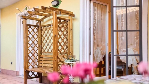 A wooden pergola structure with a lattice design, a small table with a decorative item, and a door with curtains.