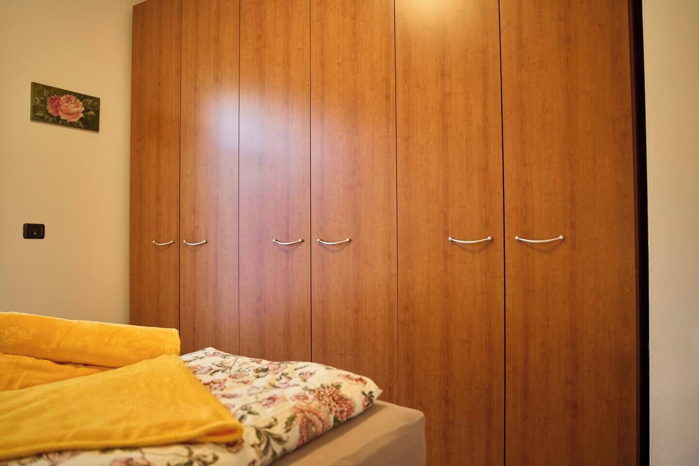 A bedroom with a wooden wardrobe, a bed with a floral bedspread, and a small painting on the wall.