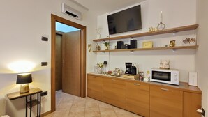 A compact kitchen with a microwave, coffee maker, and a TV mounted above a wooden shelf.