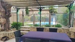 Ein überdachter Außenbereich mit Tisch und Stühlen, einer Steinmauer und Blick auf einen Swimmingpool.