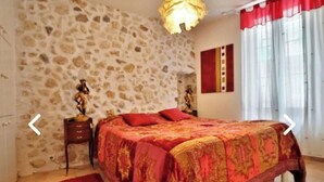 Ein Schlafzimmer mit Steinsandsteinwand, einem Bett mit roter Bettwäsche, einem Nachttisch mit Lampe und einem Fenster mit roten Vorhängen.