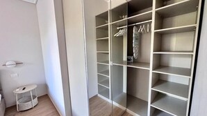 En modern garderob med flera hyllor och plats för att hänga kläder, ett litet bord med en korg och en lampa på väggen.