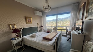 A hotel room with a large bed, a desk, a chair, and a view of the city. - Large "classic" apartment, breathtaking view. Tennis court and swimming pool nearby. (Tresserve)