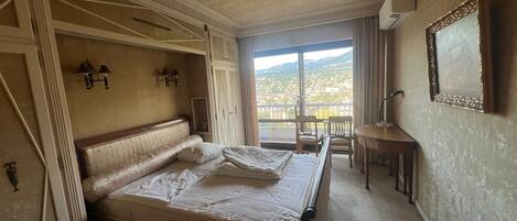 Ein Hotelzimmer mit einem großen Bett, einem Schreibtisch und Blick auf eine Stadtlandschaft durch das Fenster.