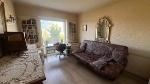 A room with a wooden desk, a purple sofa, a large mirror, and a view of trees through a window. - Large "classic" apartment, breathtaking view. Tennis court and swimming pool nearby. (Tresserve)