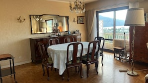 A dining area with a wooden table and chairs, a chandelier, a large mirror, and a view of the outdoors. - Large "classic" apartment, breathtaking view. Tennis court and swimming pool nearby. (Tresserve)