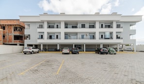 A modern multi-story building with a parking area in front. - RRC - Condominium Near the Airport (Florianópolis)
